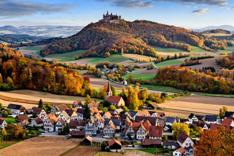Hohenzollern Castle above autumn woodland and a half-timbered village in Baden-Württemberg